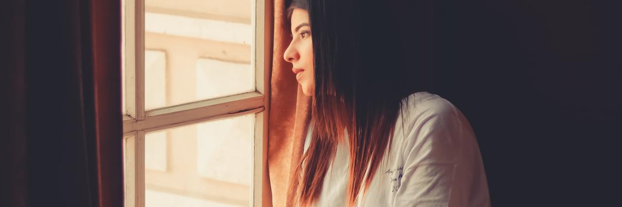 COVID-19 Isolation When You Have Bipolar Disorder and Fear Being Alone photo of a woman sitting by a window looking lonely