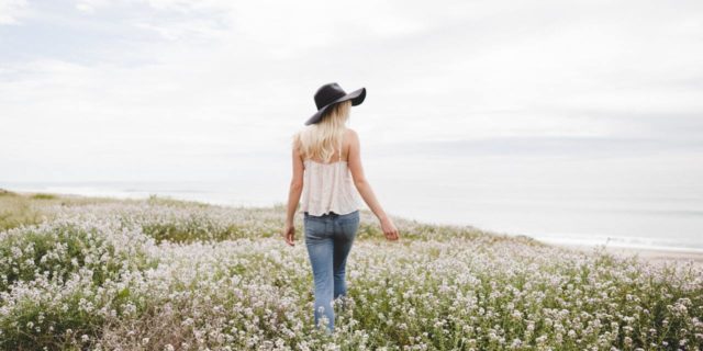A young white woman walking through a field of flowers looking behind her