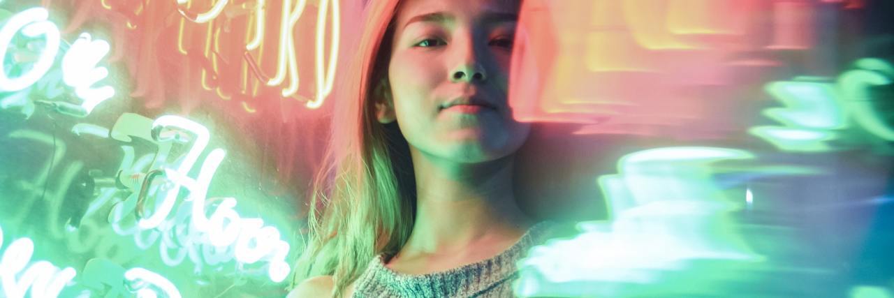 photo of young woman standing in middle of bright neon lights and lighting, arms crossed and smiling confident