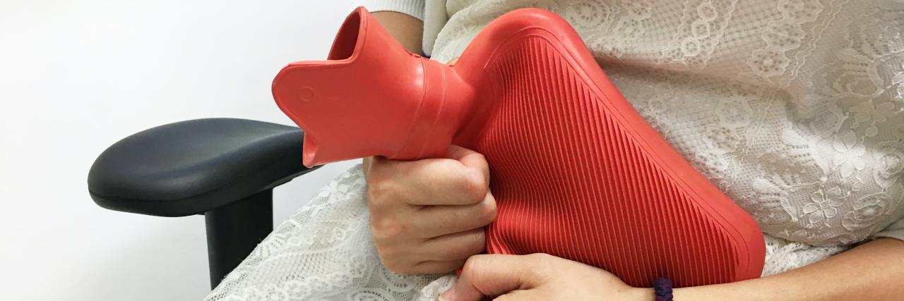My Experience With Endometriosis and Being a Sexual Abuse Survivor photo of a woman in a white dress clutching a red hot water bottle tight