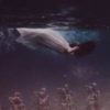 photo of a woman in a white dress swimming underwater with statues below her