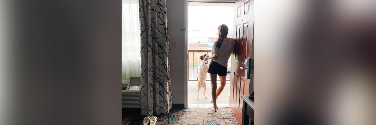 What Hurricane Ida Taught Me About Evacuation and Chronic Illness Photo of contributor standing in doorway and looking out of hotel room with her dog