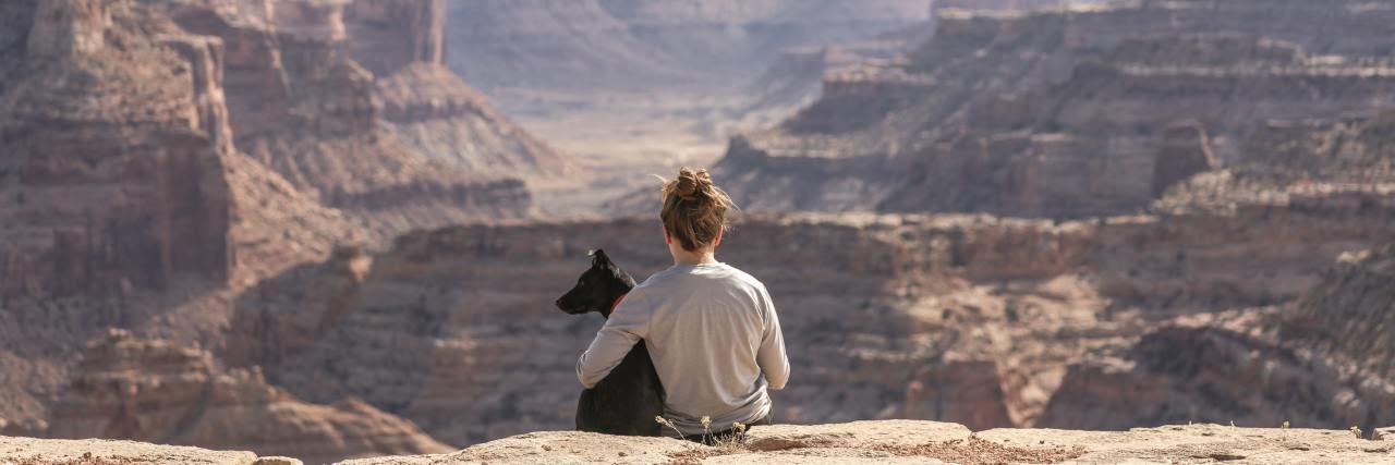 Woman sitting on a cliff with her dog, overlooking beautiful landscape