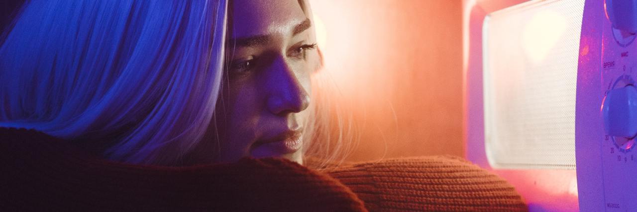 Cooking Hacks For When Illness Makes Cooking Overwhelming photo of a woman looking into a microwave with a smile