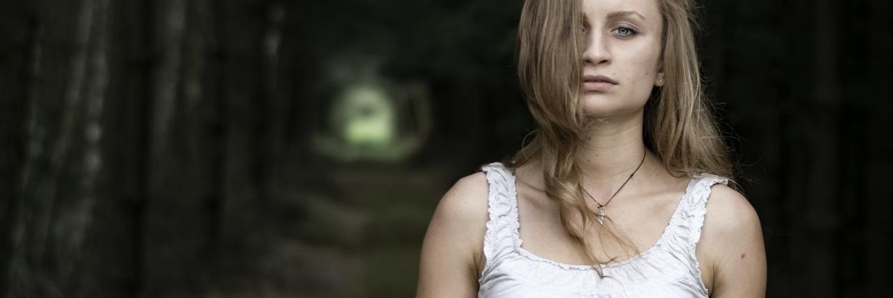 What to Know About 'Quiet' Suicide Attempts and Their Warning Signs photo of a young woman in woods looking into camera with serious expression
