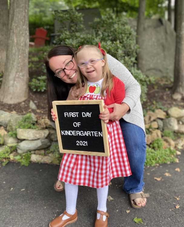 a mom and her daughter with Down syndrome holding a sign on the first day of kindergarten