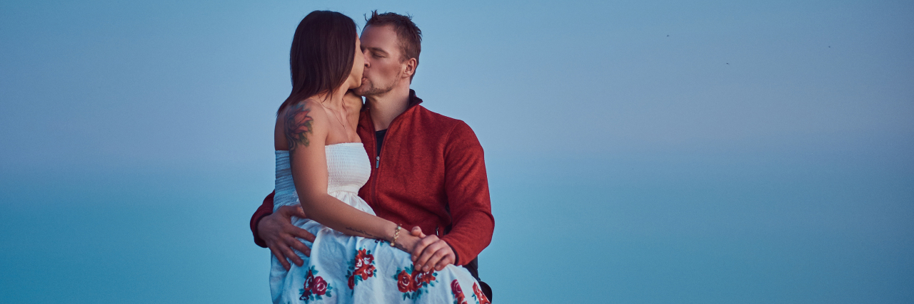 Yes, Disabled People Have Sex Woman sitting on lap of man in wheelchair. They are kissing on the beach.