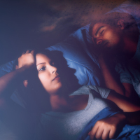 Woman laying in bed next to her husband unable to sleep.