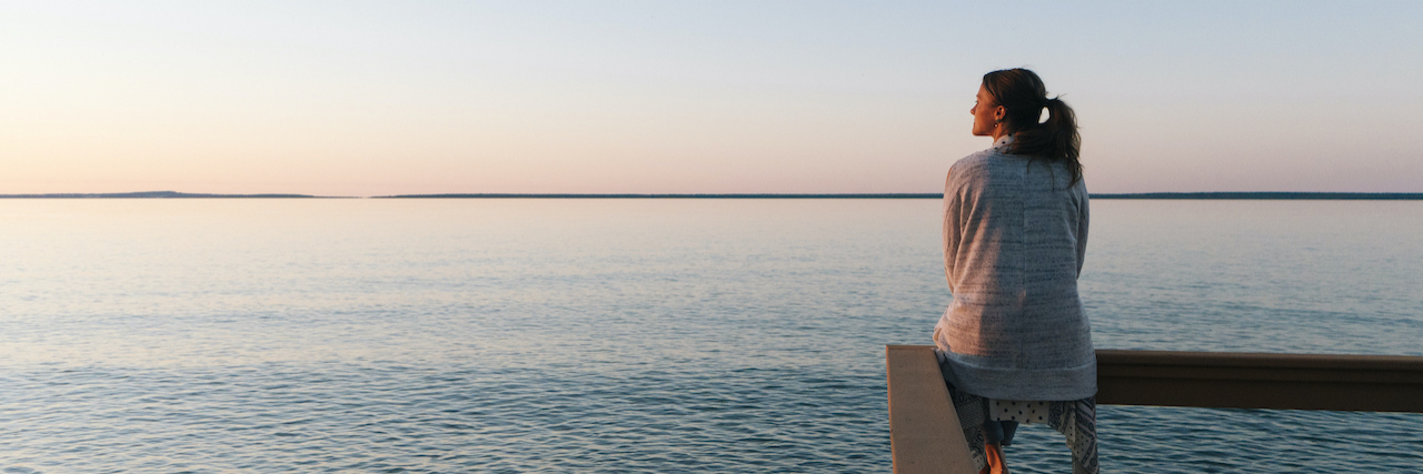 Considering Fertility, Future and Family With Life-Threatening Illness Woman sitting on fence over water at sunset