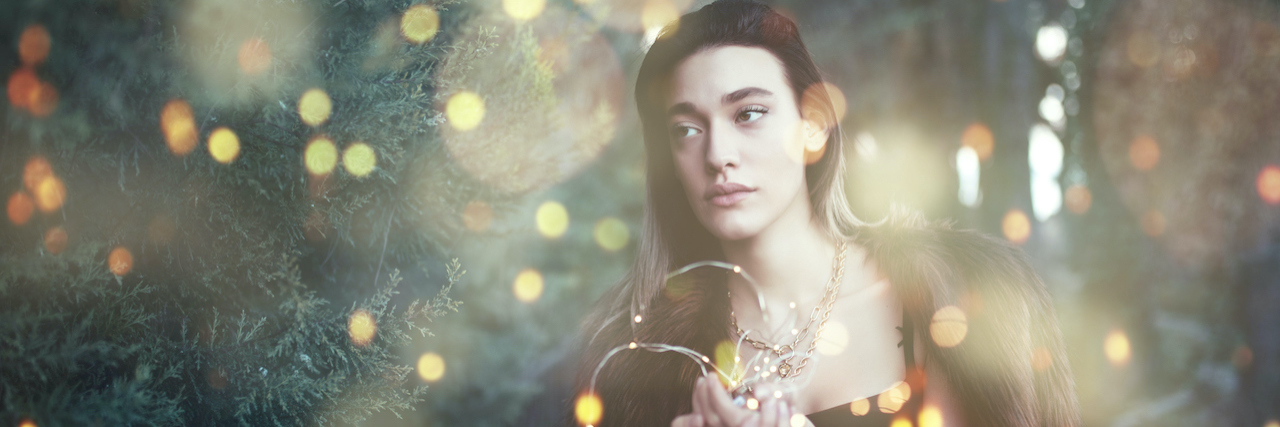 7 Tips for Surviving the Holidays With Grief A woman holding Christmas lights standing outside next to a Christmas tree