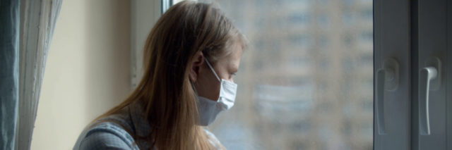 Young woman wearing a mask at home looking out the window