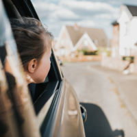 Young girl sticking her head out of the car window, looking at the houses up the street