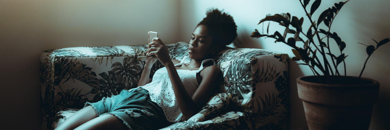 Bored woman sitting on sofa scrolling on her phone.