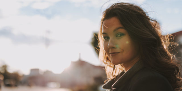 Woman gently smiling in front of city background on a sunny day