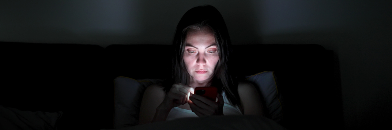 a woman sitting in the dark looking at a cell phone