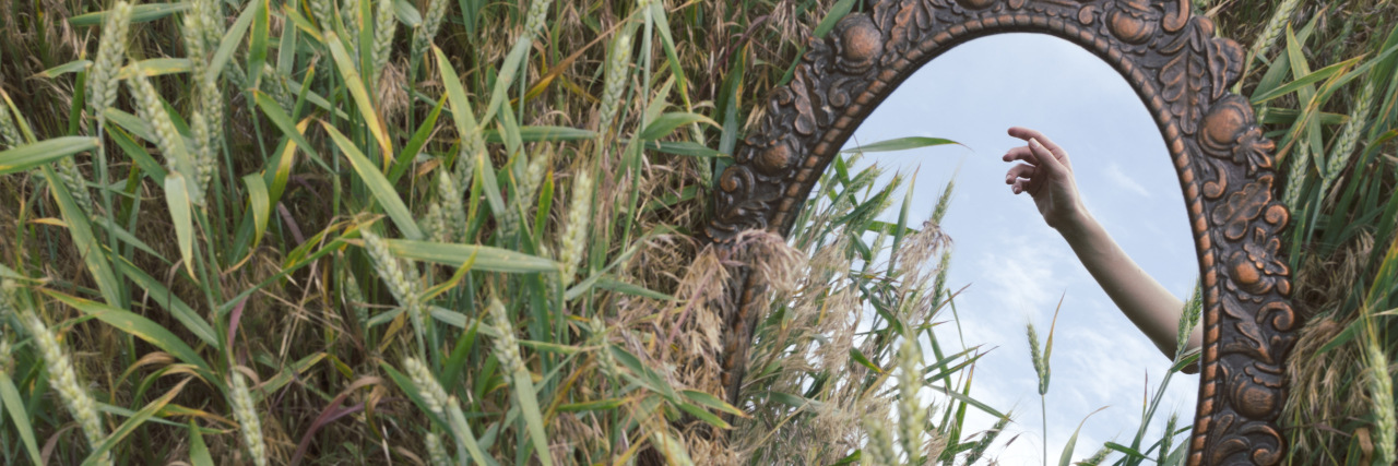 5 Secrets About My Life With an Invisible Disability Hand in reflection of an antique mirror in a field.