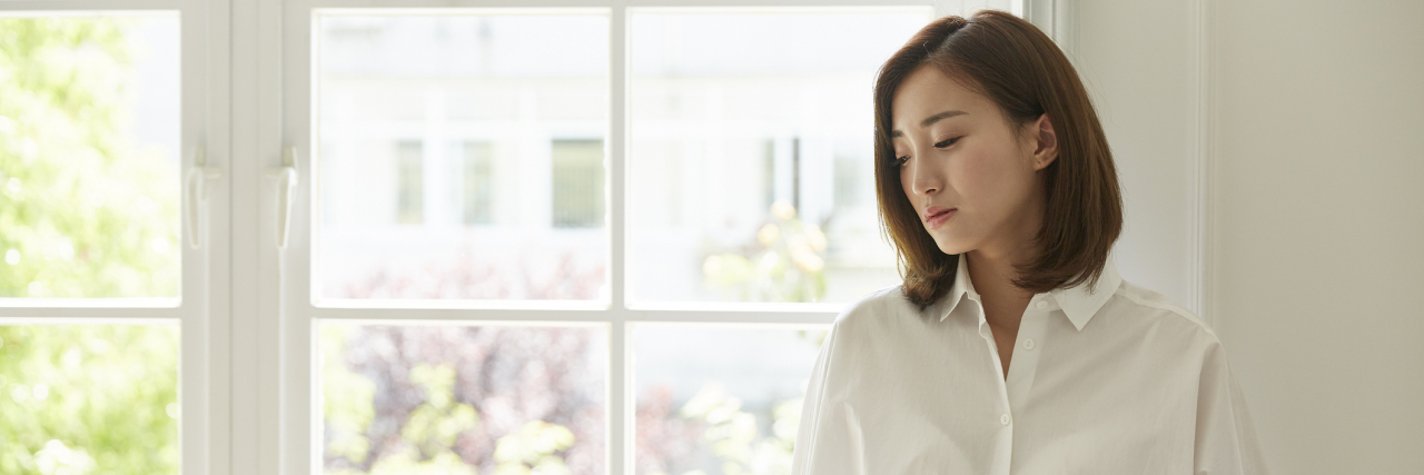 To the Person I Hurt When My Depression Left Me Desperate for Support young asian woman standing by window at home looking away, sad