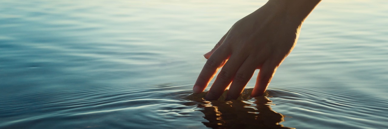 A female hand touching the ocean water at sunset.