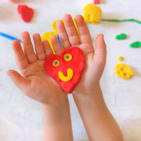 Child playing with modeling clay and sculpting heart.