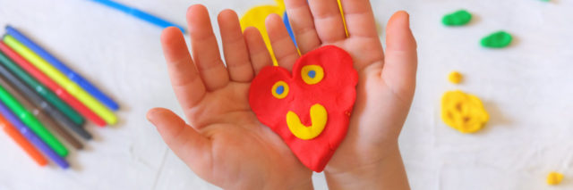 Child playing with modeling clay and sculpting heart.
