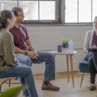 A group of four middle aged adults sit in a circle in attendance to a therapy session in urban office space.