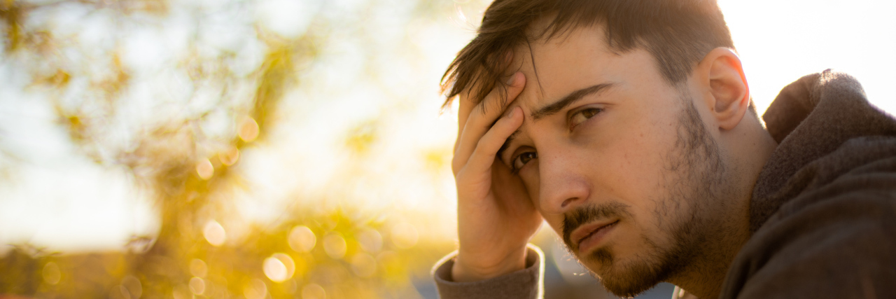 Young man sitting outside with his hand on his forehead, thinking hard