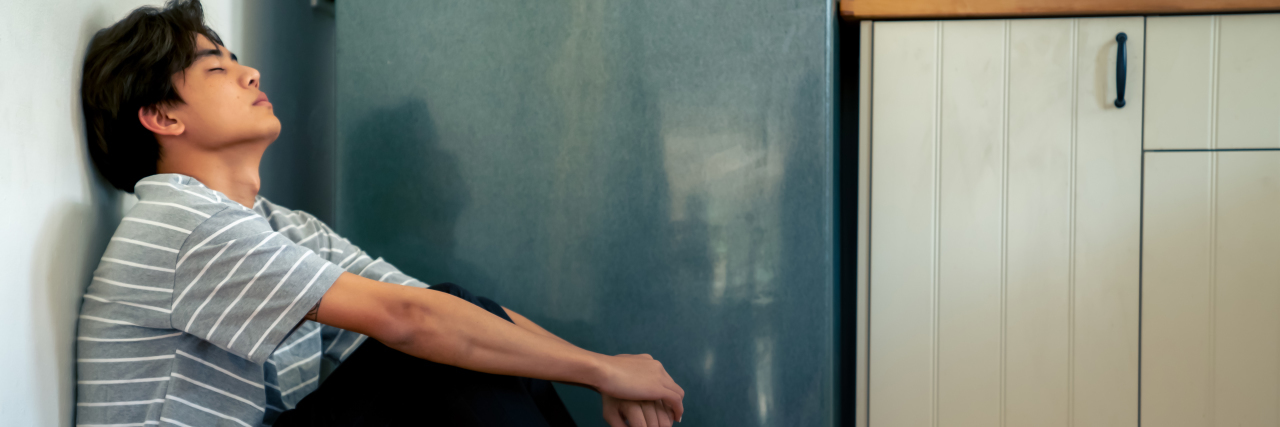 Experiencing Temporary Paralysis Because of My Movement Disorder Young Asian man sitting on the floor in kitchen.