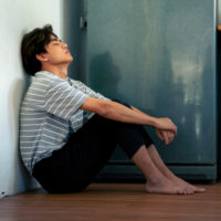 Young Asian man sitting on the floor in kitchen.