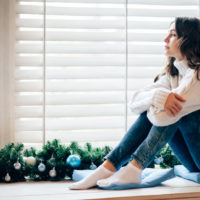 Young woman in a sweater sitting on a window sill, looking off into the distance
