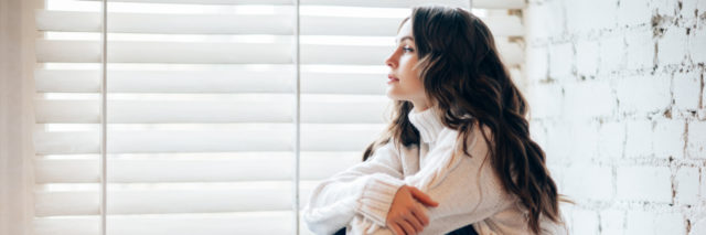 Young woman in a sweater sitting on a window sill, looking off into the distance