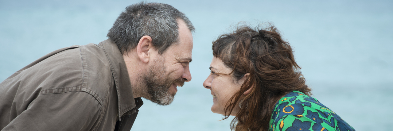 A man and woman by an ocean looking at each other smiling