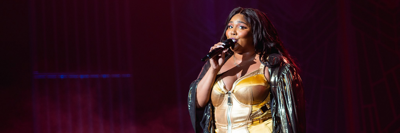 Lizzo singing at a concert, wearing a gold costume.