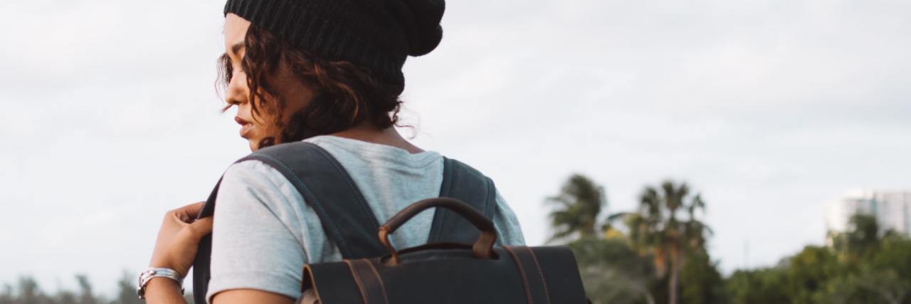 Mental Health Service Wait Times at College Are Too Long photo of a young woman facing away from camera with backpack and black hat