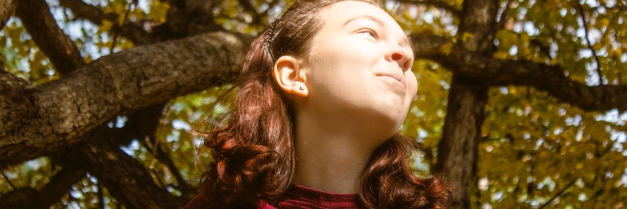 photo of a woman taken from below with tree overhead, she's looking off to the distance with eyes squinted against sun