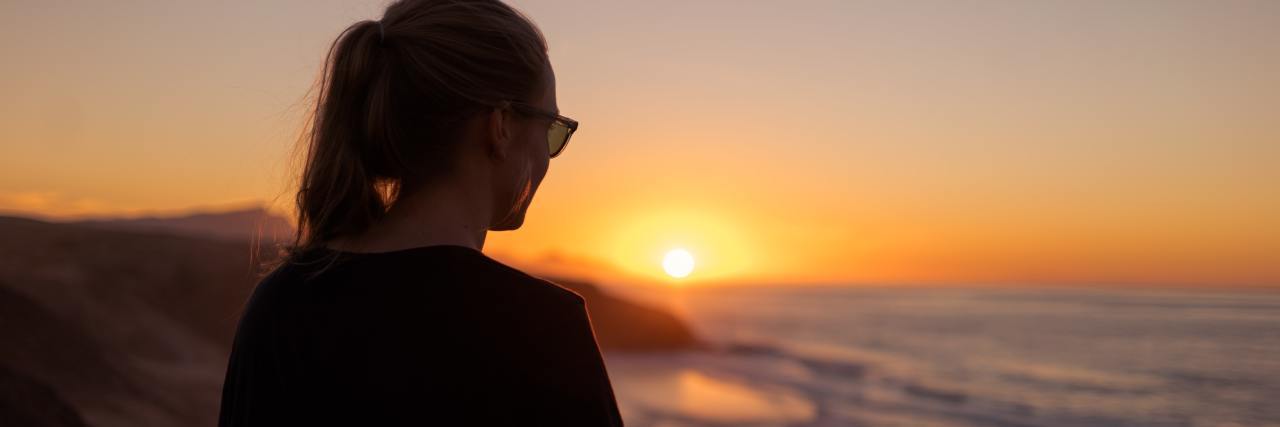 photo of a woman standing on a shoreline at sunset looking out at the ocean