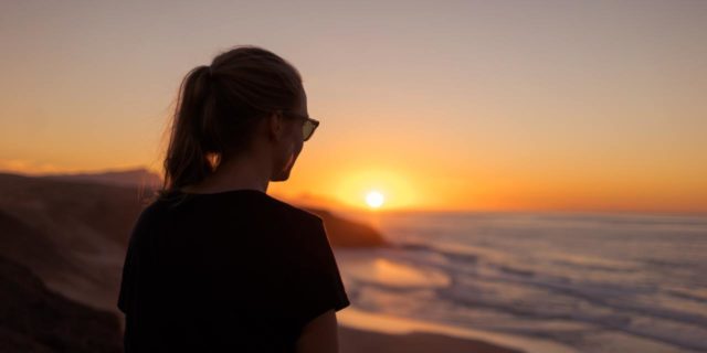 photo of a woman standing on a shoreline at sunset looking out at the ocean