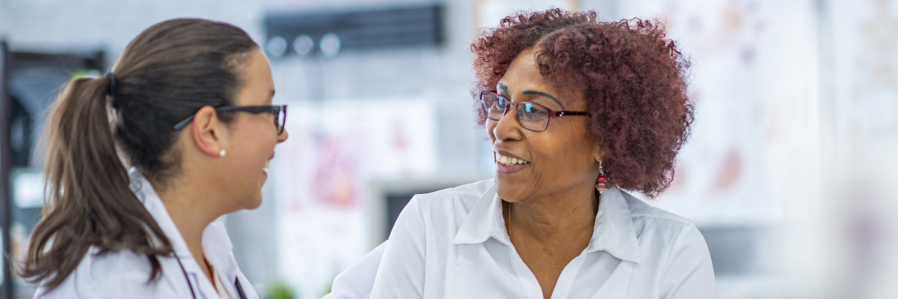 Best Non-Medical Advice Doctors Have Given People With Chronic Illness A Black woman smiles as she talks with a doctor sitting beside her at a medical office