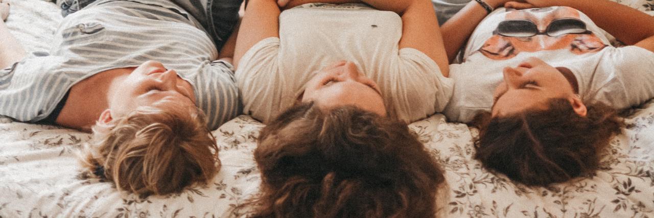 Real Ways to Help Someone With Psychosis or Schizoaffective Disorder photo of three friends lying down together with legs upright, smiling and chatting