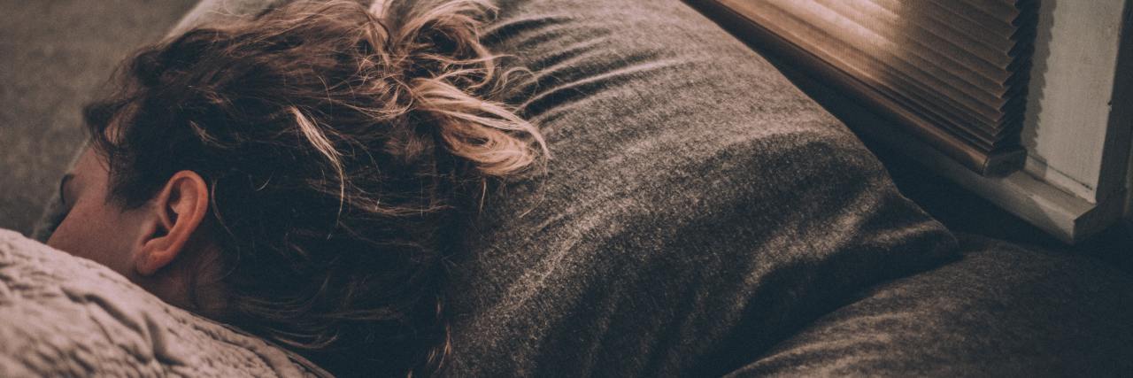 How I Survive Wanting to Die By Suicide Immediately After Waking Up photo of a young woman lying in bed facing away from camera