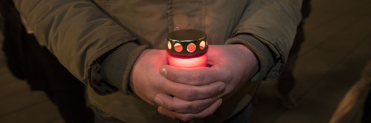 Mourning Disability Rights Advocates on Disability Day of Mourning Close-up photo of a man in a brown jacket holding a candle.
