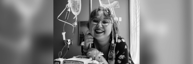 Black and white image of Megan smiling and holding onto an IV pole during treatment