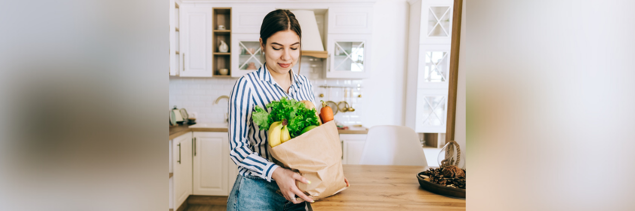 Woman holding brown bag full of fresh vegetables in kitchen