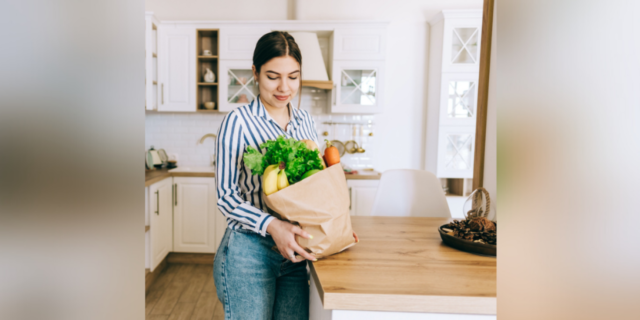Woman holding brown bag full of fresh vegetables in kitchen