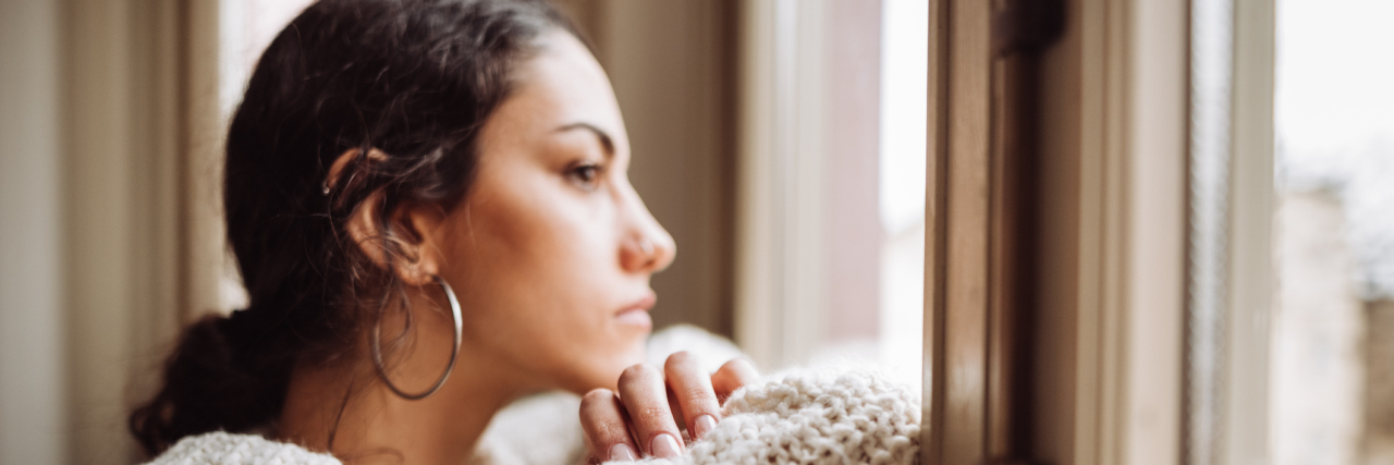 How COVID-19 Helped Me Realize I Needed Better Friends Young woman in a thick sweater looking outside the woman, curious