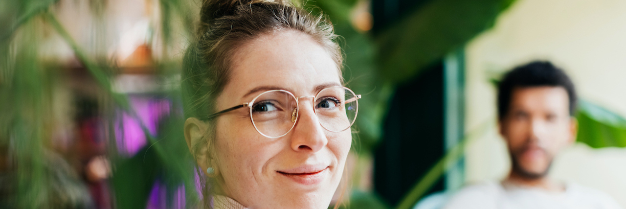 Preparing for and Dealing With OCD Flares During Holiday Travel Portrait of a woman sitting by green plants and slightly smiling