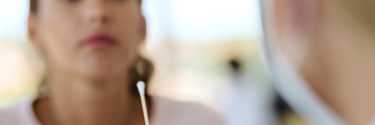 How Worrying About COVID Exposure Messes With My OCD Healthcare worker using a cotton swab to do a coronavirus with a woman blurred in the background