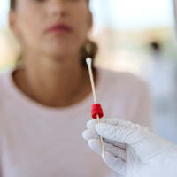 Healthcare worker using a cotton swab to do a coronavirus with a woman blurred in the background