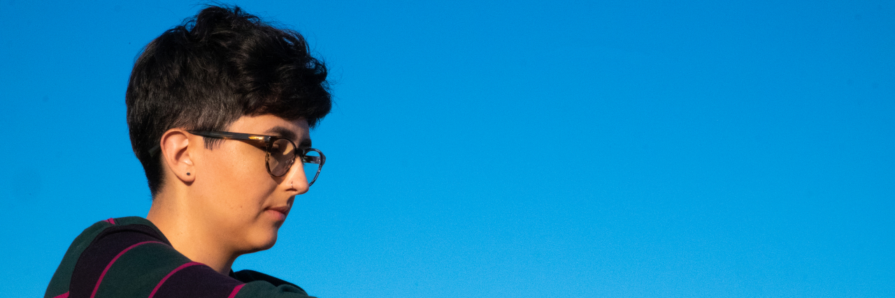 Why Coming Out as Autistic Was Harder Than Coming Out as Queer A non-binary person sitting in a field near mountains.
