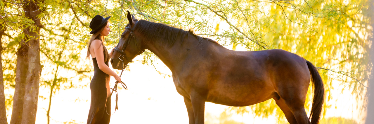 Learning to Advocate for Myself With Post-Concussion Syndrome Woman stands with a horse in the forest at sunset.