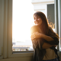 Woman standing next to window, smiling with sunlight coming in
